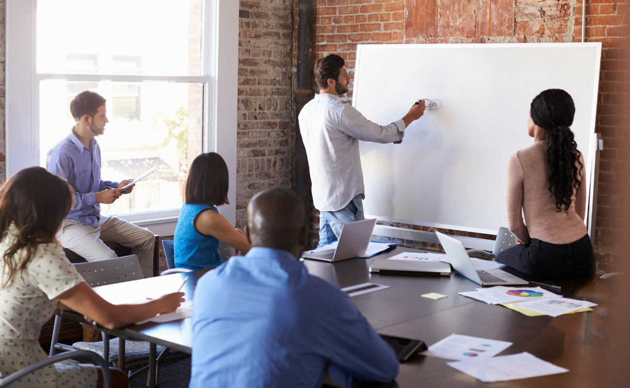 Man teaching on whiteboard to a group of people.