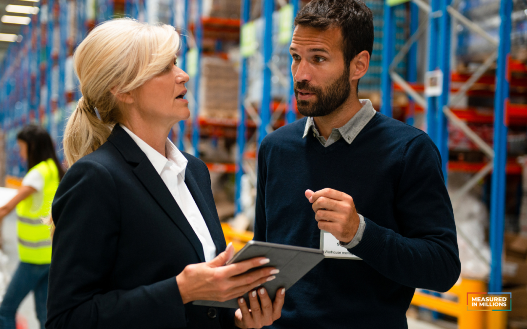 Man and woman in business attire talking in a warehouse.