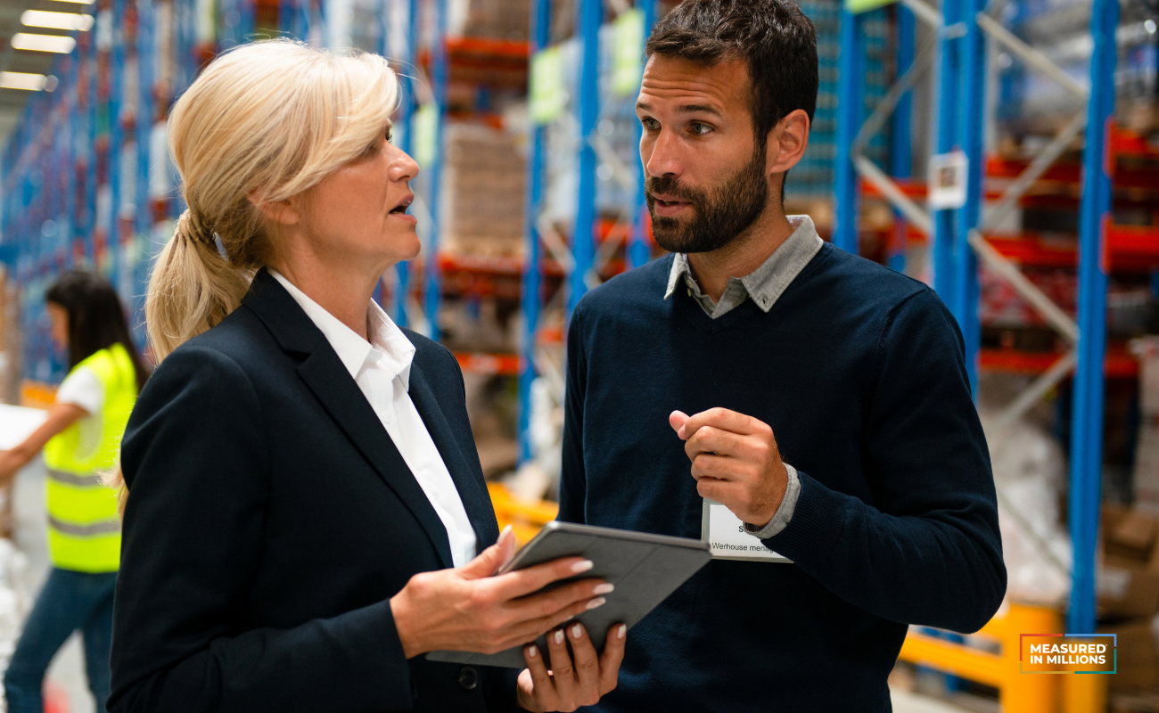 Man and woman in business attire talking in a warehouse.