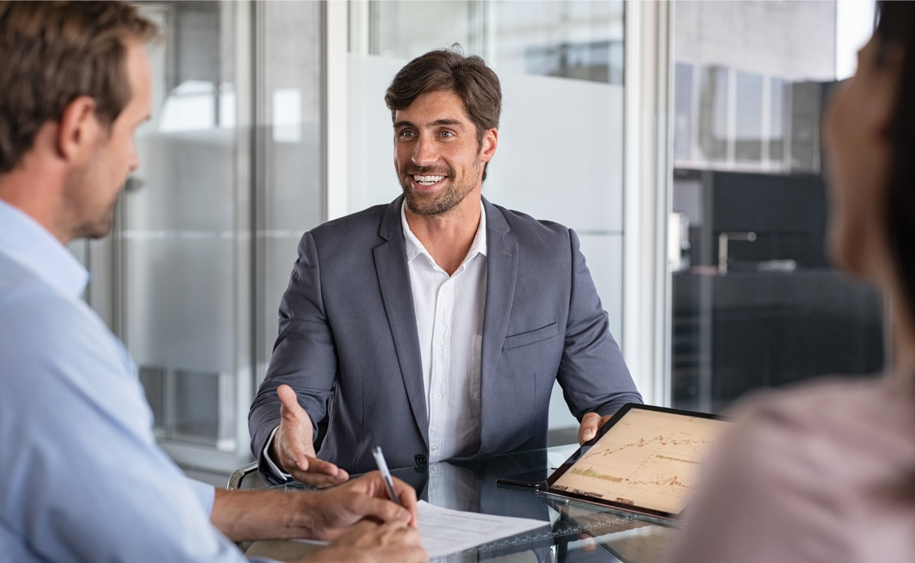 Man in business casual presenting to 2 people with a tablet.